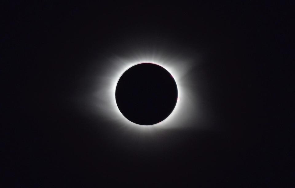 Eclipse solar total con la corona brillante alrededor del disco negro de la Luna. En el centro hay un círculo completamente oscuro y, rodeándolo, un halo blanco y difuso que se extiende de forma suave hacia el fondo negro, representando la corona del Sol.